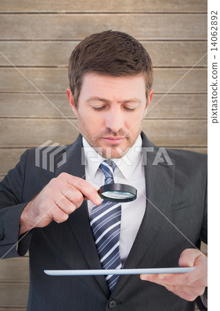 Composite image of businessman looking at tablet with magnifying 14062892
