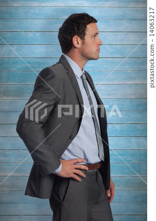 Composite image of serious businessman with hand on hip 14063217