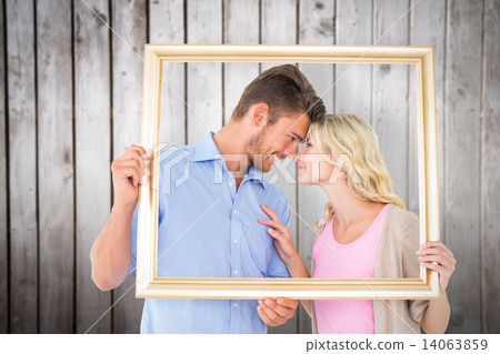 Composite image of attractive young couple holding picture frame 14063859