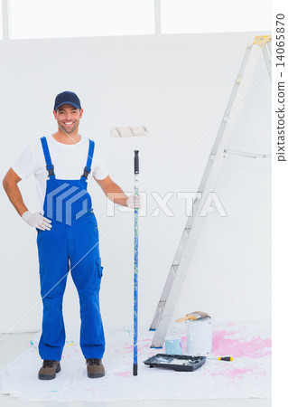 Handyman in overalls holding paint roller at home Handyman in overalls holding paint roller at home 14065870