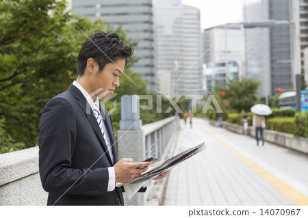 A busy businessman image manipulating smartphones while watching English newspapers 14070967