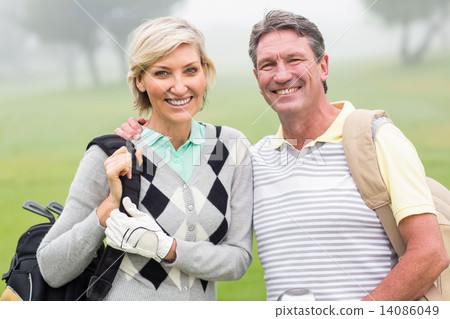 Golfing couple smiling and holding clubs Golfing couple smiling and holding clubs 14086049