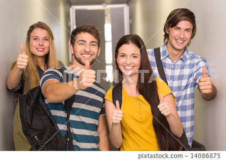 Happy students gesturing thumbs up at college corridor Happy students gesturing thumbs up at college corridor 14086875