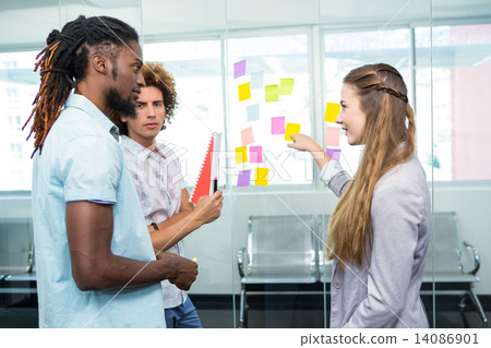 Creative team pointing at adhesive notes in office 14086901