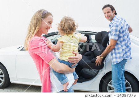 Parents carrying baby and her car seat Parents carrying baby and her car seat 14087379