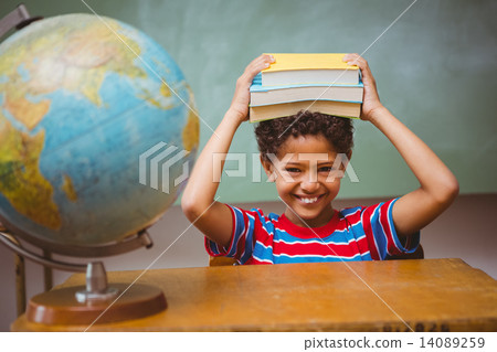 Little boy holding books over head in classroom 14089259