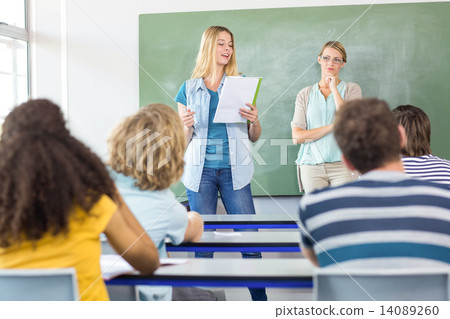 Student explaining notes besides teacher in class 14089260