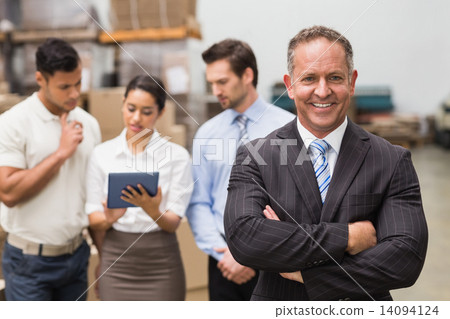 Boss standing with arms crossed in front of his employees 14094124
