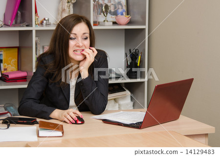 Nervous girl in office bites his nails, working on computer 14129483