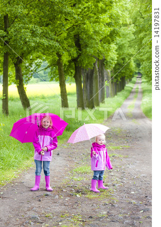 little girls wearing rubber boots with umbrellas in spring alley 14197831