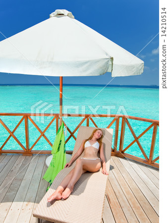 Young woman tans on a water villa terrace , Maldives 14210514