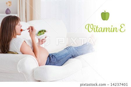 Vitamin e against pretty pregnant woman eating a salad while lyi 14237401