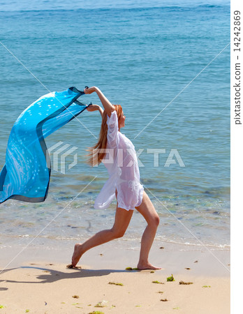 The young attractive woman on the sea coast with a blue scarf in hands.. The young attractive woman on the sea coast with a blue scarf in hands.. 14242869