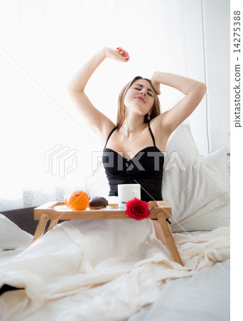 Beautiful woman sitting in bed and stretching while having break Beautiful woman sitting in bed and stretching while having break 14275388