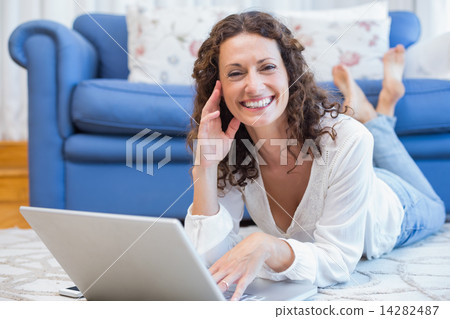 Smiling woman lying on the floor and using her laptop Smiling woman lying on the floor and using her laptop 14282487
