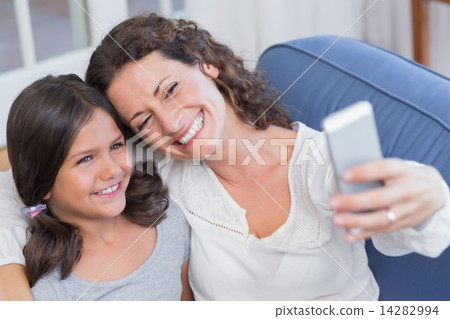 Happy mother and daughter sitting on the couch and taking selfie Happy mother and daughter sitting on the couch and taking selfie 14282994