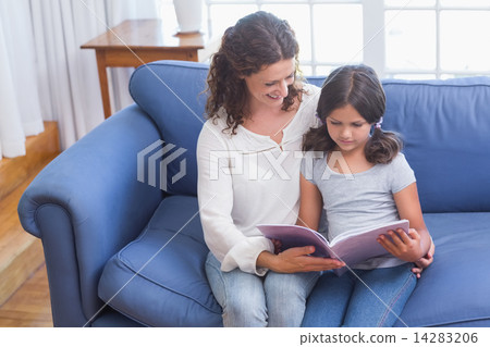 Happy mother and daughter sitting on the couch and reading book 14283206
