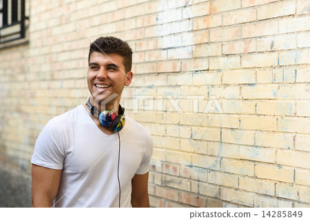 Young man in urban background listening to music with headphones Young man in urban background listening to music with headphones 14285849