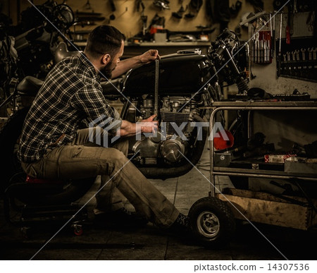 Mechanic building vintage style cafe-racer motorcycle  in custom garage 14307536