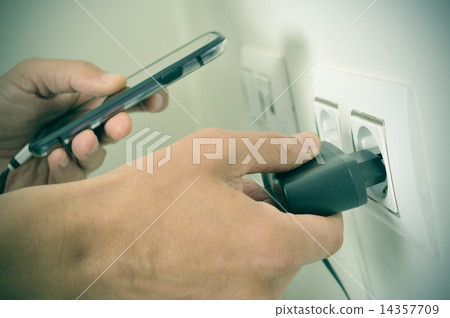 man plugging in the plug of his smpartphone in a socket, with a man plugging in the plug of his smpartphone in a socket, with a 14357709