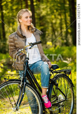 Cheerful teenage girl listens music on a bicycle outdoors Cheerful teenage girl listens music on a bicycle outdoors 14387374