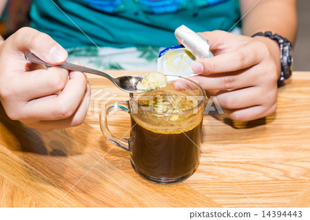 Person adding butter to black coffee 14394443