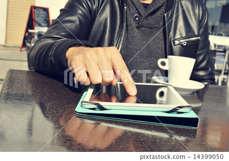young man with a cup of coffee using a tablet in the terrace of young man with a cup of coffee using a tablet in the terrace of 14399050