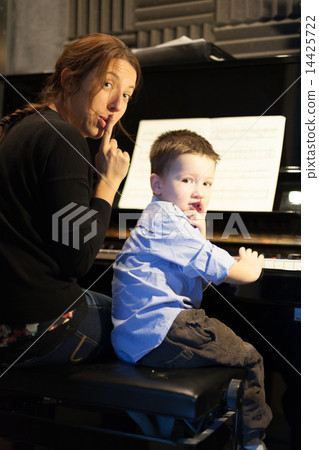 Boy putting index finger on lips with his piano instructor Boy putting index finger on lips with his piano instructor 14425722