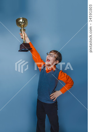 European-looking  boy of  ten  years in glasses holding a cup award on a blue background 14591803