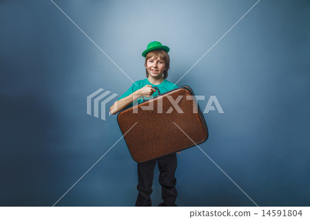 European-looking boy of ten years in a hat holding a suitcase in hand, itinerary on a blue backgroun European-looking boy of ten years in a hat holding a suitcase in hand, itinerary on a blue backgroun 14591804