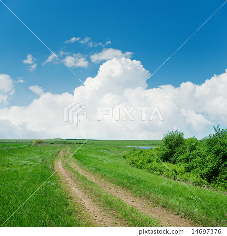dirty road in green landscape and clouds over it 14697376