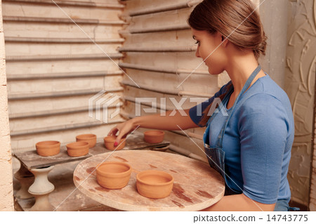 Woman puts clay pots on the shelf 14743775