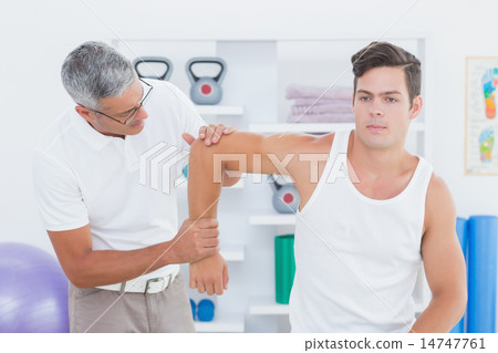 Doctor stretching a young man arm Doctor stretching a young man arm 14747761