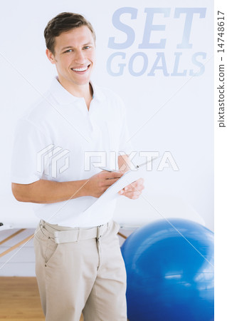Composite image of smiling male trainer with clipboard in gym at Composite image of smiling male trainer with clipboard in gym at 14748617