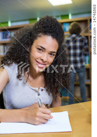 Student writing notes in notepad in the library 14748868