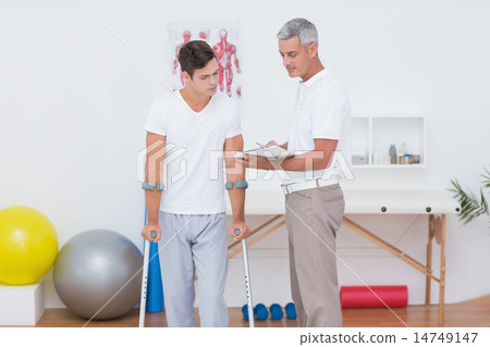 Doctor showing clipboard to his patient with crutch Doctor showing clipboard to his patient with crutch 14749147