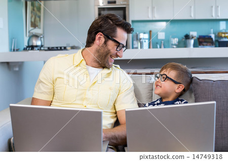 Father and son using laptops on the couch Father and son using laptops on the couch 14749318