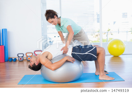 Trainer helping man with exercise ball Trainer helping man with exercise ball 14749319