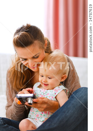 Young mother showing her smiling baby photos on camera 14787619