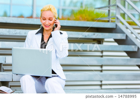 Smiling business woman sitting on stairs talking on mobile and l Smiling business woman sitting on stairs talking on mobile and l 14788995