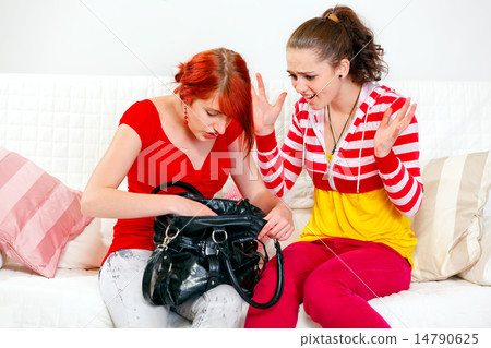 Indignant girl sitting on sofa and looking on searching something in handbag girlfriend. Indignant girl sitting on sofa and looking on searching something in handbag girlfriend. 14790625