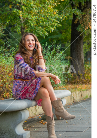 Smiling young woman talking cell phone in city park 14790714