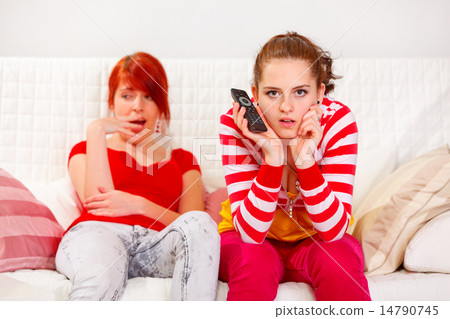 Bored girl yawning while her girlfriend attentively watching TV Bored girl yawning while her girlfriend attentively watching TV 14790745