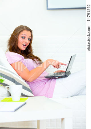 Confused pretty woman sitting on couch and pointing finger at laptop. 14791262