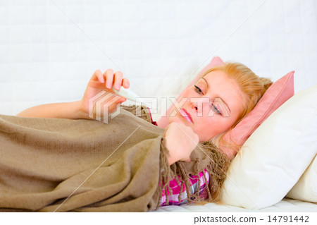 Ill woman laying on bed and looking on thermometer Ill woman laying on bed and looking on thermometer 14791442