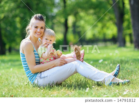 Happy mother and baby sitting on grass in park Happy mother and baby sitting on grass in park 14791812