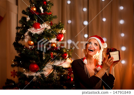 Interested woman near Christmas tree shaking present box trying Interested woman near Christmas tree shaking present box trying 14791849
