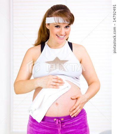 Smiling beautiful pregnant woman wiping her belly with towel after exercising at home. 14792491
