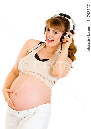 Smiling pregnant woman holding her belly and listening music in headphones . Smiling pregnant woman holding her belly and listening music in headphones . 14792737