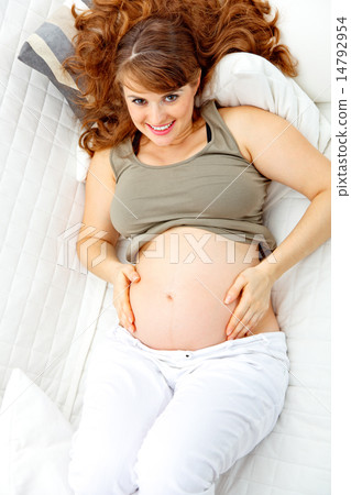 Happy beautiful pregnant woman relaxing on couch and holding her belly. 14792954